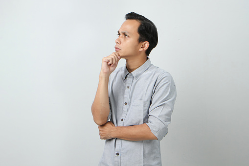 Pensive young Asian Indonesian man with a serious face thinking about a question, thoughtful about confusing idea on isolated background
