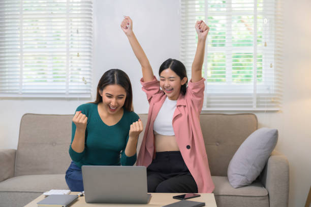 istock Two joyful women working together with laptop computer while sitting on the sofa, freelance, work from home concept. 2057542021