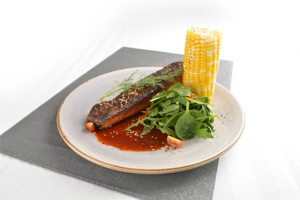 pan fried bbq fresh cod, salmon, grouper fish fillet in chef sauce with potato, corn and vegetables in plate on white table restaurant luxury hotel western cafe halal menu