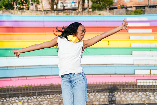 Carefree woman with headphones enjoys a moment of freedom by a pride wall.