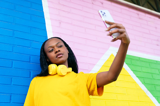 Trendy afro woman with headphones snapping a selfie, vivid background.
