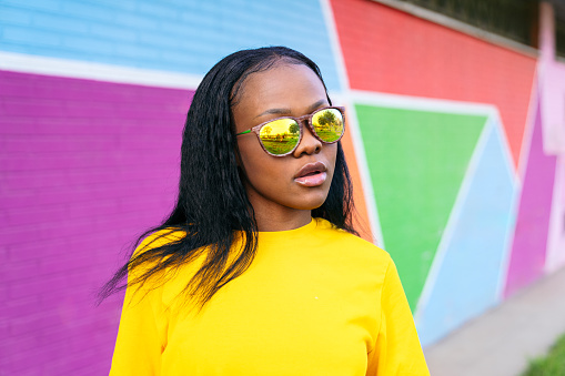 Stylish afro woman in reflective glasses, colorful urban backdrop.
