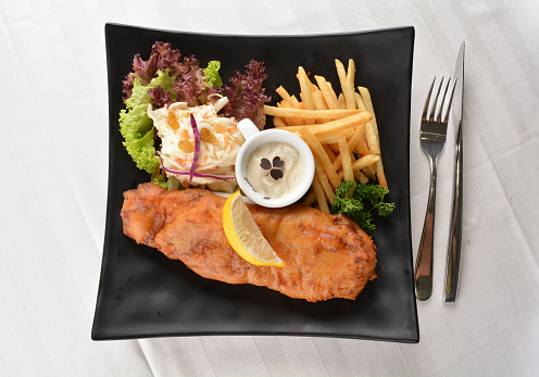 chef deep fried golden fish and chips with tartar sauce, lemon , French fries and salad dressing in plate on white table restaurant luxury hotel western cafe halal menu