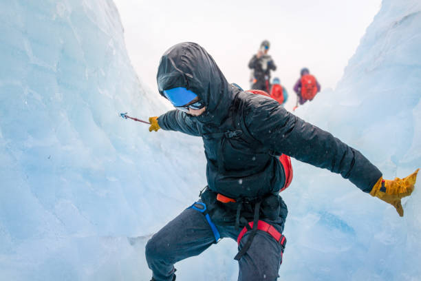 Man climbing down the glacier crevasse using ropes. Unrecognizable person taking photos using a smartphone. Exit Glacier ice hiking. Alaska.
