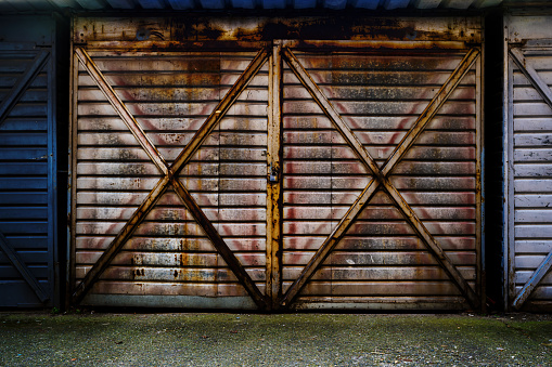 Old metallic garage door made of corrugated steel metal sheets locked with padlock, worn and rusty surface