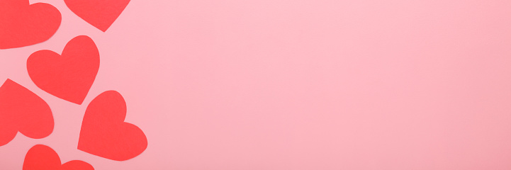 Red heart shapes from application paper on light pink table background. Pastel color. Love concept. Wide banner. Closeup. Empty place for text. Top down view.