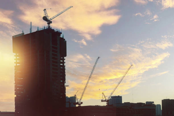 Dramatic image of silhouette architectural building at construction site with tower cranes on summer colorful twilight sky for business, technology and industry presentation background.