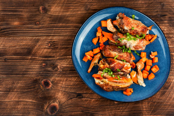 Stock photo showing close-up, elevated view of  a traditional roast chicken dinner served for Sunday lunch on an oval, green serving plate, featuring juicy roasted chicken, golden potatoes, pigs in blankets (pork cocktail sausages wrapped in bacon), sliced carrot and tender Brussels sprouts. This stock image highlights hearty home-cooked meals, comfort food, and family dining.