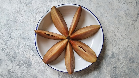 Sapodilla (Manilkara zapota) cut in slices on rustic white background. Manilkara zapota, commonly known as sapodilla, sapote, chicozapote, chicoo, chicle, naseberry, nispero, or soapapple
