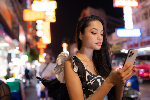 Portrait of asian female tourist with mobile phone on night walk in the Chinatown area of Bangkok, Thailand