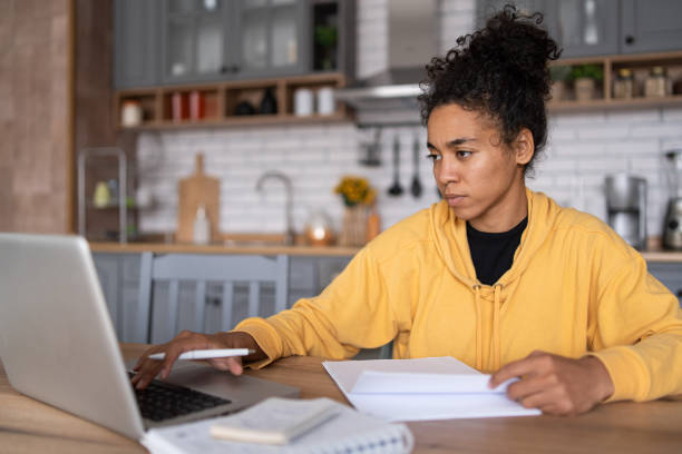 istock An african-american young woman is using laptop computer for remote work or studying online, she takes notes watching webinars or classes at kitchen table at home 2057671740