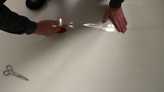 A man sticks a transparent wide tape to the joint of two polyester sheets of insulation for the floor, gluing the edges of a soft substrate under the laminate, do it yourself