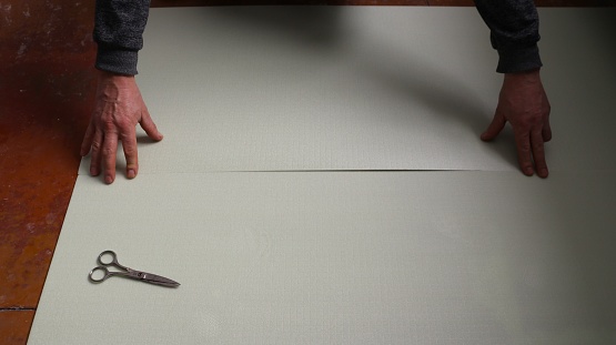 a man connects two greenish polyester sheets on the floor, making an insulated layer before laying the laminate, a soft underlay under the laminate in the room during the covering process
