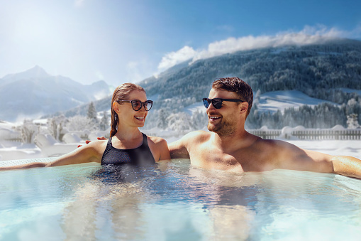 happy couple relaxing in outdoor hot tub at ski spa resort. winter vacation