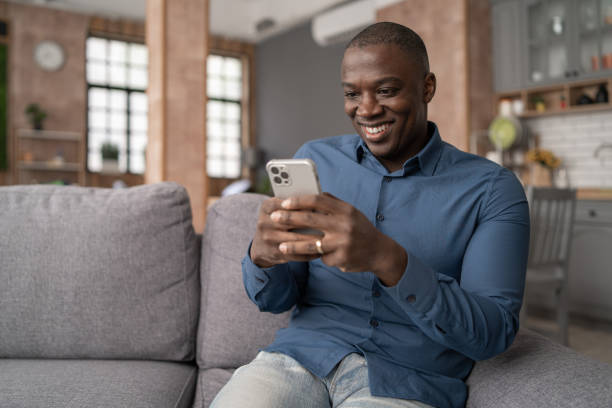 istock Excited Black African American Man Using Smartphone for mobile shopping while Sitting on the Sofa in Living Room. Happy Man buying things, shopping online 2057677861