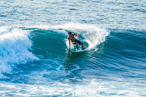 Bali, Uluwatu - A surfer, balanced on a surfboard, rides a turquoise wave. Blue ocean in the background.