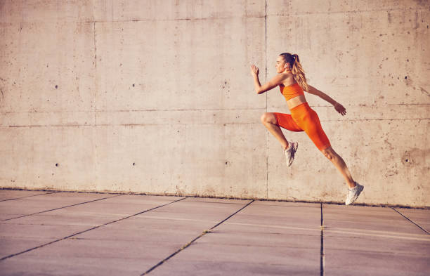 Athletic woman running with concrete wall in background