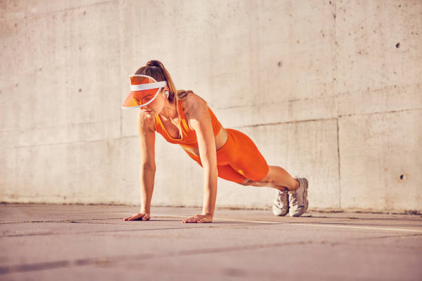 Athletic adult woman doing pushup exercise outdoors against concrete wall stock photo