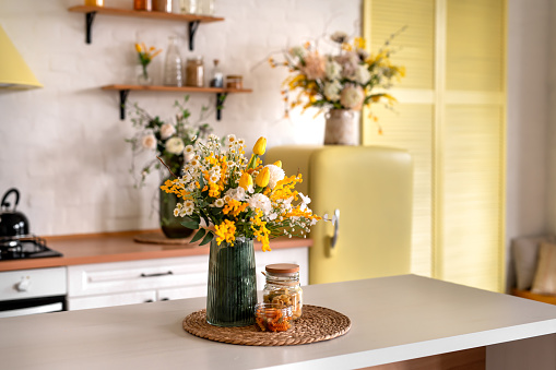 A bouquet of flowers on a wooden table. In the background, the interior of a white kitchen in the Scandinavian style. The concept of home comfort