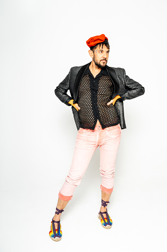 A man showcases his unique style in a black leather jacket, dotted shirt, and pink pants paired with colorful rainbow footwear.