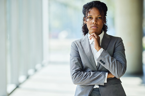Portrait of serious African American businesswoman standing in a hallway of an office building and looking at camera. Copy space.