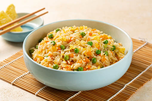 Fried rice with egg and vegetables, onion, bell pepper, carrot, green peas. Prepared and served in a light blue plate, chopsticks.