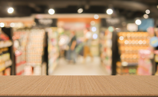 blur local supermarket convenience store background with beige wood perspective tabletop to showing product or ads banner and promote  marketing on display concept