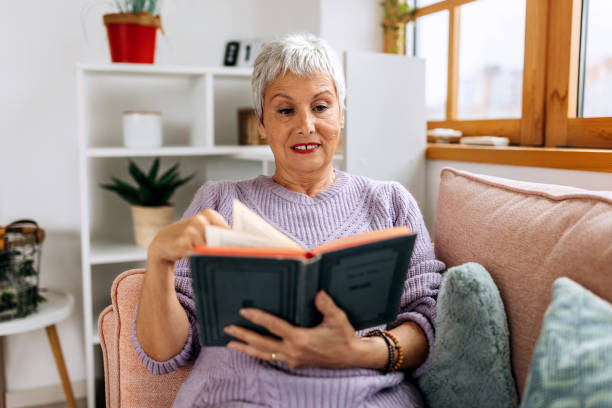 istock Senior woman reading book while sitting on a sofa at home 2057742246