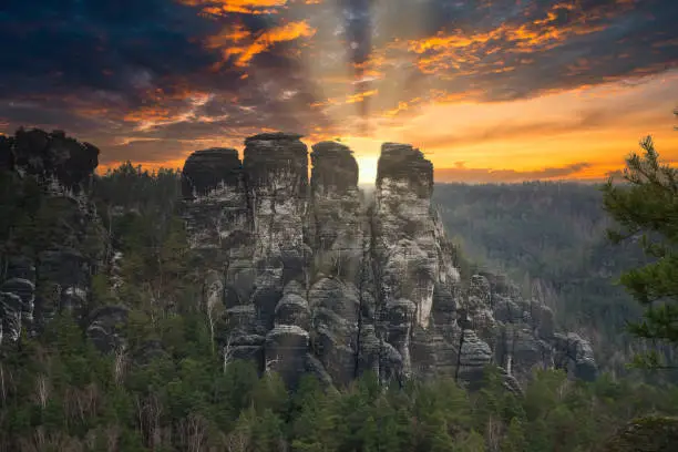 Rugged rocks at Basteibridge at sunset. Wide view over trees and mountains. National park in Germany