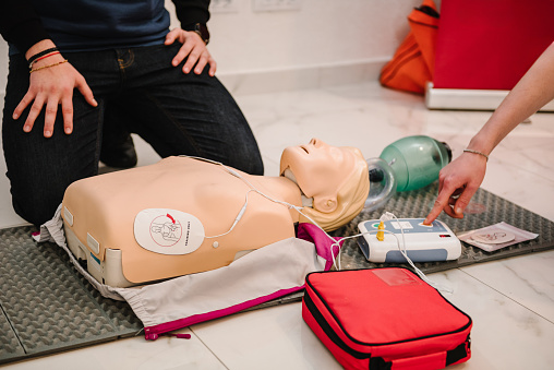 Use an automatic defibrillator in conducting basic cardiopulmonary resuscitation of victim. Automated external defibrillator device, AED with training dummy mannequin. Demonstrating chest compressions