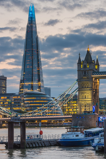 View across the River Thames to the historic span of Tower Bridge beneath the sunset sky overlooked by the futuristic glass spire of The Shard in the heart of London, Britain's vibrant capital city.