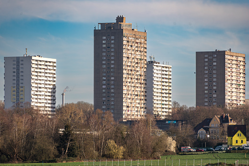 Telephoto shot of three residential silos with windows, balconies, antennas in the afternoon sunlight with unleafy trees in the foreground and light cloud cover