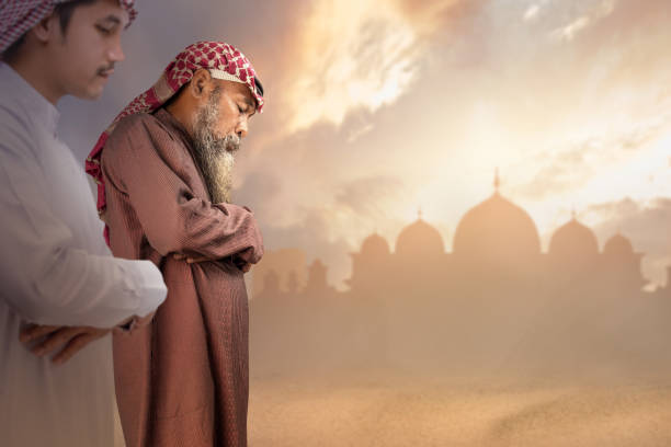 Two Muslim men with agal in a praying position (salat) with a dramatic sky background. Muslim concept
