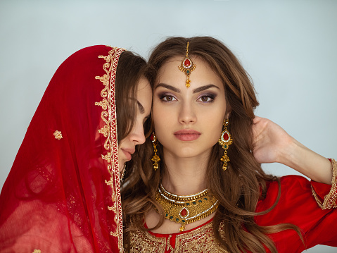 Beauty portrait of two Indian girls in red bridal sari posing in studio. Young hindu women models jewelry set. Traditional Indian costume