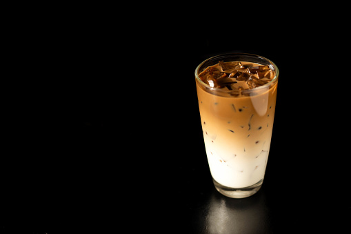 Glass of ice latte coffee with on black background. Cold beverage in summer.