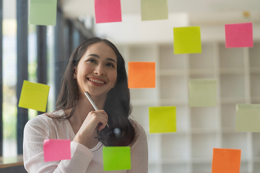 Asian businesswomen use post-it notes on glass walls to write strategic business plans for development to grow to success.