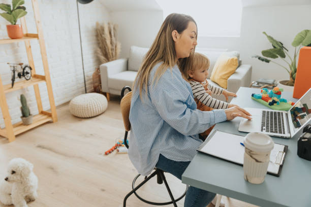 istock Young mother working on laptop from home office while holding her baby son on lap 2057825240