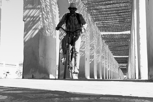 Cycling outdoors in a footpath with arched walls arcade roof covered with sorghum stalks, sunny day with shadows. Surface level view with grayscale colors contrasted.
