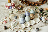 Happy Easter! Stylish easter eggs, bunnies and cherry blossom on rustic table. Modern natural dyed and chocolate colorful eggs and spring flowers. Easter still life decor in countryside home