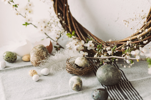 Happy Easter! Stylish easter eggs in nest and cherry blossom on rustic table. Modern natural dyed marble eggs and spring flowers. Easter still life decor in countryside home