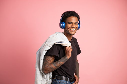 Studio portrait with pink background of a cool man holding jacket on shoulder listening to music with headphones