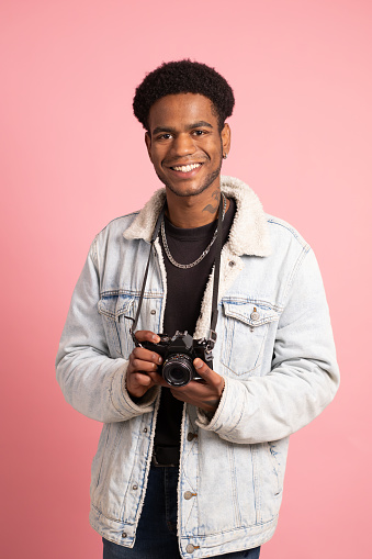Studio portrait with pink background of an african young man with a digital camera