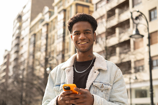 Portrait of a Young african man using phone smiling at camera in the city