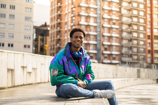 Portrait of a casual sportive man sitting on urban square smiling at camera