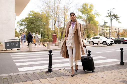 Carefree businesswoman walking on the city street while pulling her luggage.