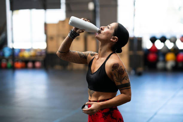 Tired strong mature sportswoman drinking water from a flask indoors stock photo