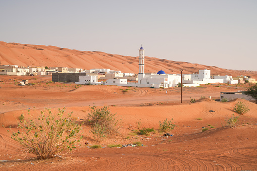 Desert village in Wahiba desert in Oman, with mosque in  center and dunes, sky in background.
