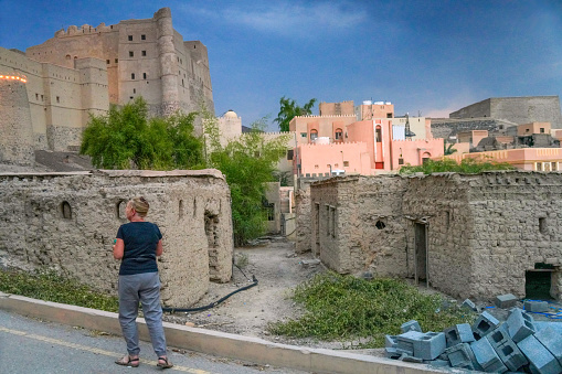 Senior woman, tourist, looking at the  ruins of village with historic Bahla Fort in background, Oman.