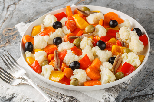 Festive Italian cauliflower salad with giardiniera, olives and anchovies close-up on a plate on the table. Horizontal
