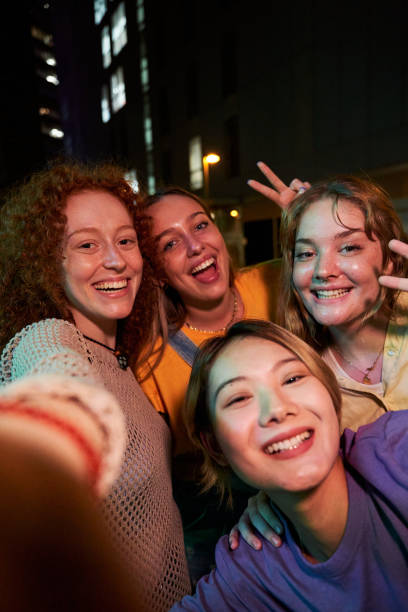 istock Young female friends taking a vertical selfie looking at camera smiling gathering at night outdoors. 2057933526